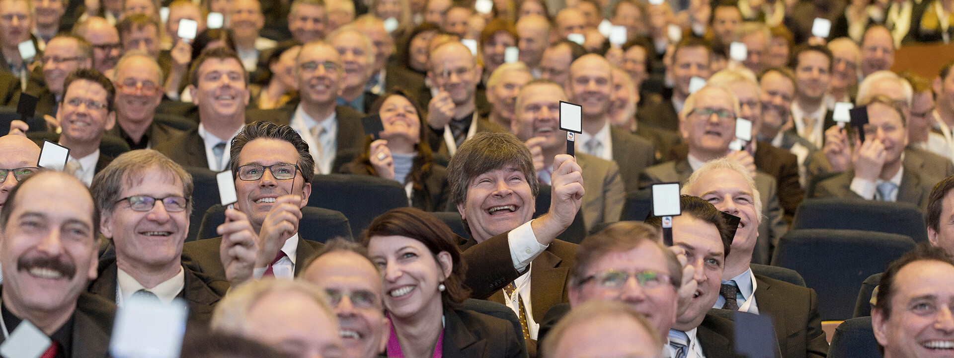 Blick auf einen vollbesetzten Konferenzraum bei einer Corporate Conference, mit Fokus auf die Präsentationsbühne.